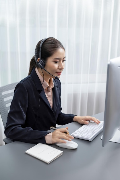 Enthusiastic asian call center with headset and microphone working on her laptop