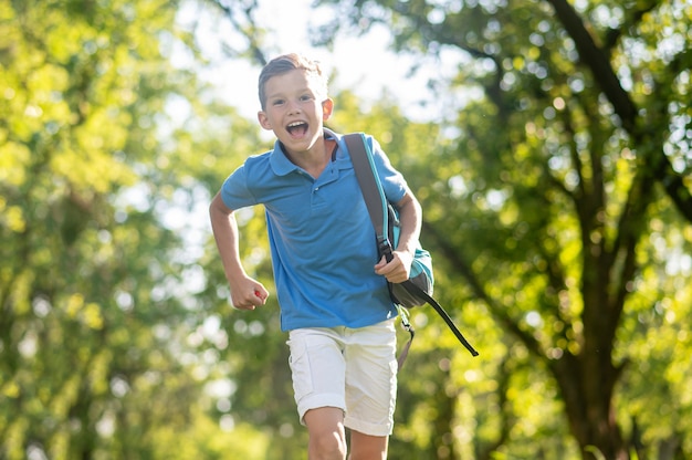 Ragazzo entusiasta con la borsa di scuola che corre nel parco