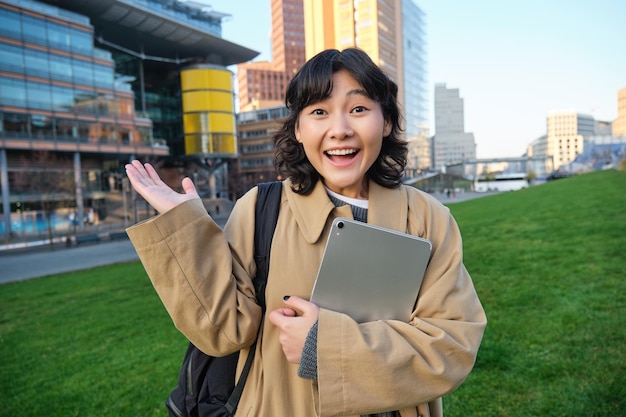 Photo enthusiastic brunette asian girl student with digital tablet in her hands looks impressed and surpri