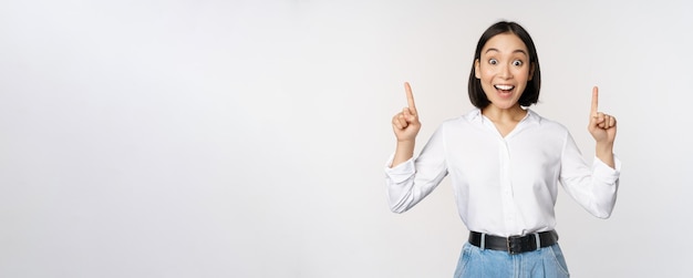 Enthusiastic business woman asian female model pointing fingers up and smiling making announcement s