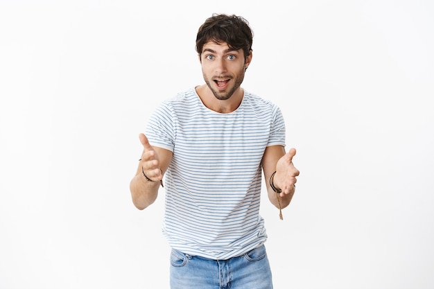 Enthusiastic and excited attractive young male model with blue eyes and bristle explaining something with thrilled surprised expression being impressed gesturing at front with happy look