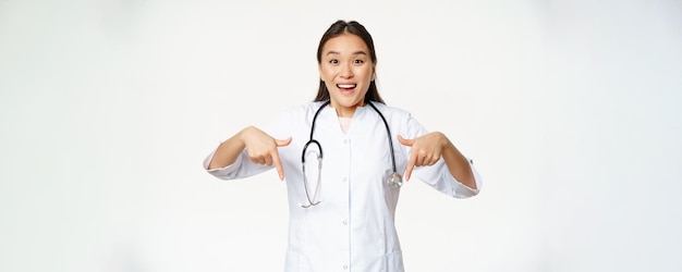 Enthusiastic medical staff asian female healthcare worker pointing fingers down and smiling amazed s