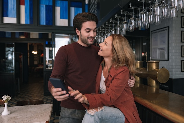 Photo enthusiastic optimistic couple using phone and staring at each other