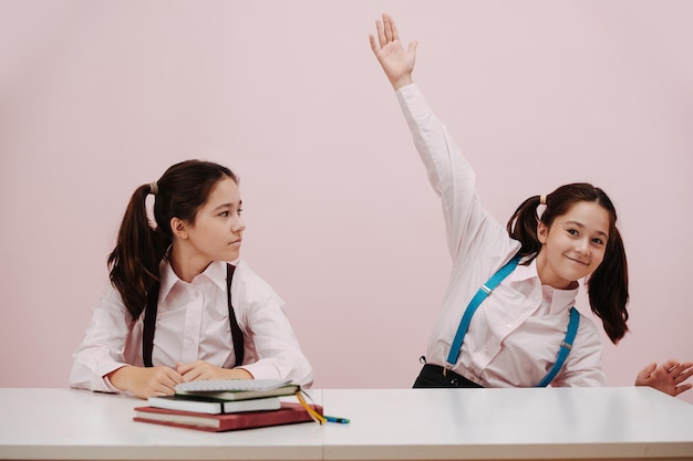 Enthusiastic perky schoolgirl raising a hand her twin eyeing her with suspition