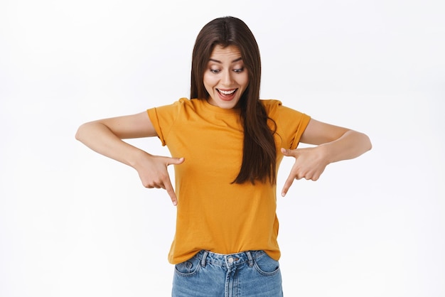 Enthusiastic wondered and amused happy woman taking part interesting event watching cool performance standing white background look and pointing down at advertisment white background