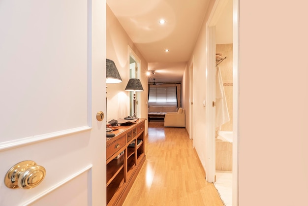 Entrance hall of the house with floating oak flooring access to a bathroom with a bathtub a wooden sideboard with drawers and a white lacquered access door