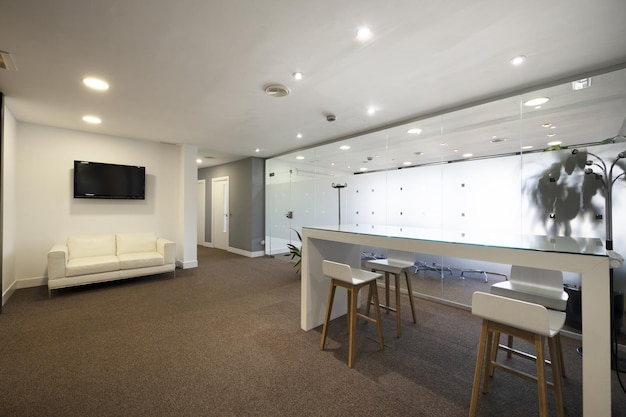 Entrance hall of an office with a white leather sofa a high table with stools and carpeted floors