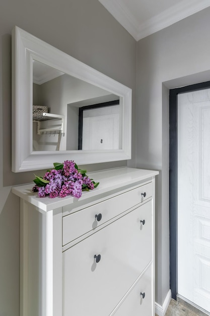 The entrance to the house with a white door and a cabinet on which lies a bouquet of lilacs