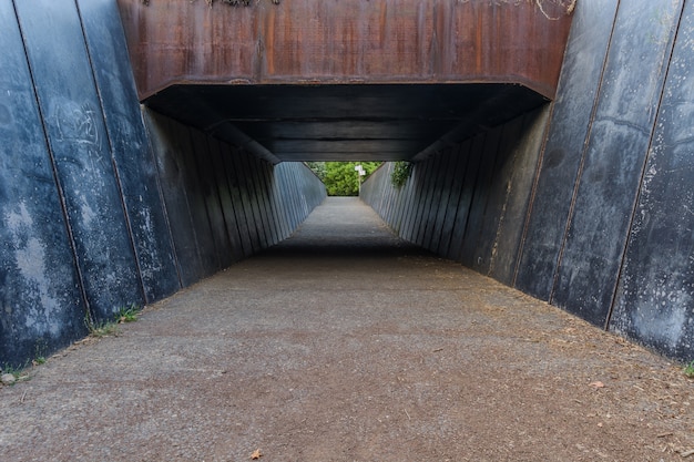 Photo entrance to a metal tunnel with its blue walls & garnet ceiling at olot, spain