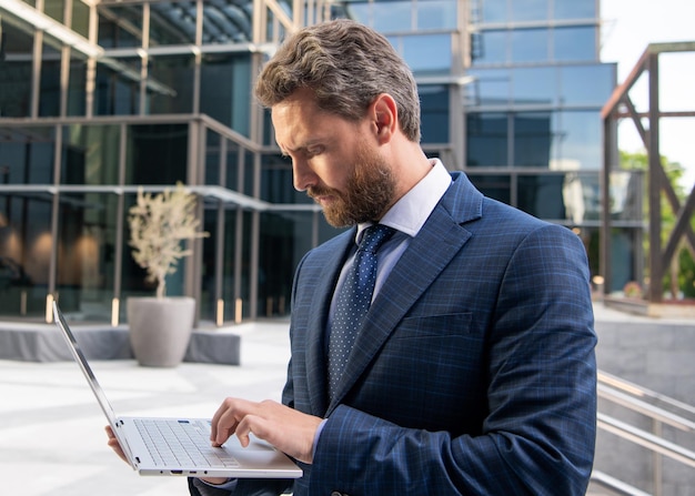 Entrepreneur in businesslike suit typing on pc outside the office modern life