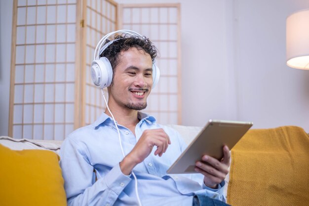 Entrepreneur businessman comfortable sitting relax lifestyle sofa couch listening music modern headphones technology tablet at indoor home apartment adult man smiling joy fun digital tablet earphones