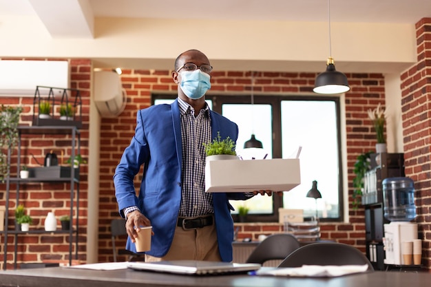 Entrepreneur gathering office belongings after getting fired from job during covid 19 pandemic. Business man holding box to pack up desk things and leave company work, being dismissed.