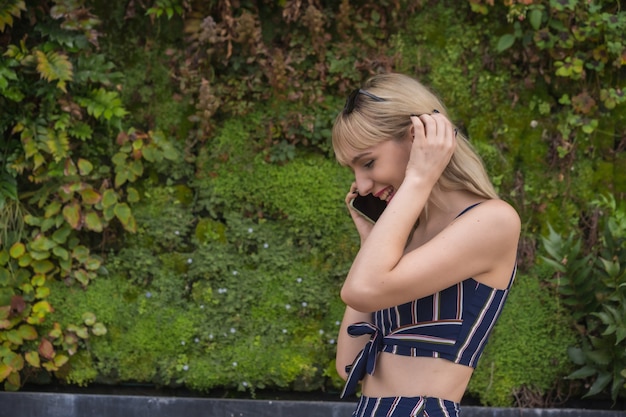 Предприниматель девушка в бизнес-парке на зеленой стене растений, молодая блондинка улыбается, звонит по телефону