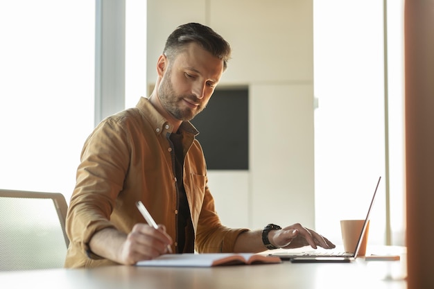 Entrepreneur man taking notes and using laptop sitting in office