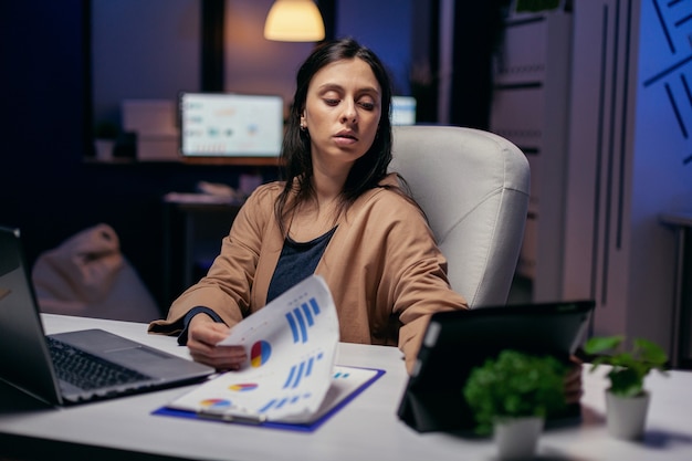 기업가는 늦은 밤 마감을 마치려고 하는 동안 터치패드에서 수입 메시지를 읽고 있습니다. 태블릿 PC를 사용하여 회사 일을 끝내기 위해 사무실에서 초과 근무를 하는 비즈니스 여성.