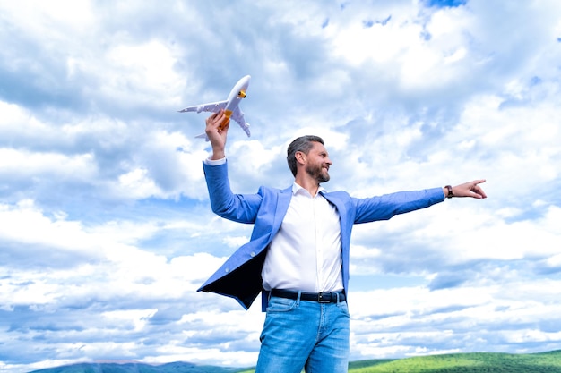 Entrepreneur ready for trip. freedom. mature boss with plane on sky background. confident businessman. fly idea. smiling man with toy plane. business success. successful man in suit dreaming.