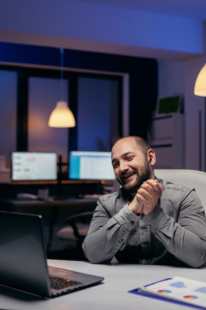 Entrepreneur smiling during business video call with someone,. late at night. Businessman in the course of an important video conference while doing overtime at the office.