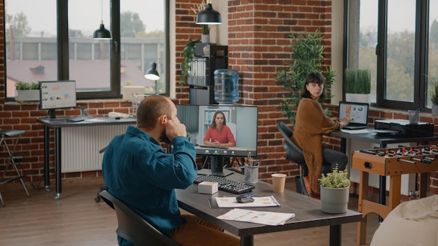 Entrepreneur using earpods to talk to manager on video call in startup office. Business man talking to woman on remote online video conference on computer to plan project and strategy.