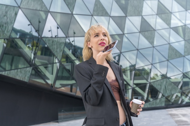 Entrepreneurial girl business park in a modern building with colored glass, young blonde woman in suit sending a voice note