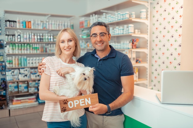 Imprenditori che tengono un cane bianco dopo aver aperto il proprio negozio di animali