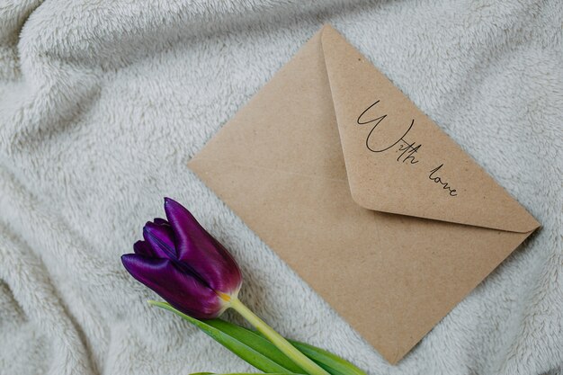 Envelope of craft paper and one purple tulip on beige plaid, envelope with love, mail envelope.