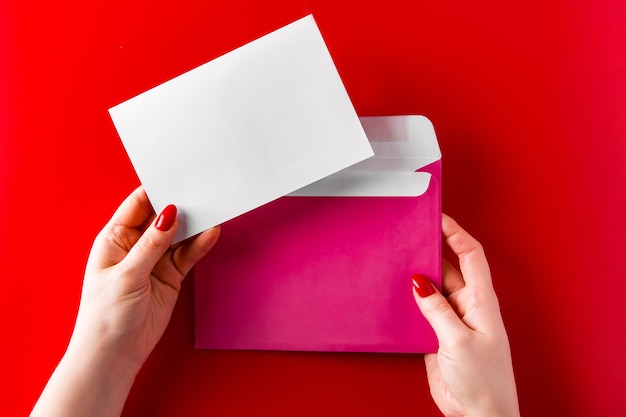 envelope in the hands of a young woman on a red background. Pink envelope and greeting card in hands on a red background.