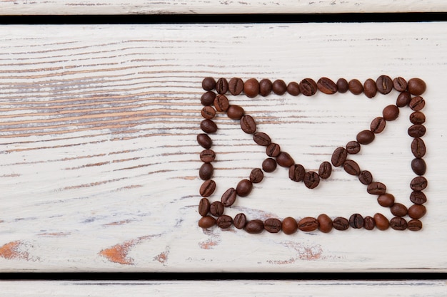 Envelope symbol made of coffee beans on white wood. Brown grains arranged in a shape of mail envelope.