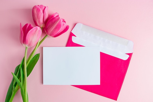 Envelope with invitation to holiday and  bouquet of tulips on pink background Place for text