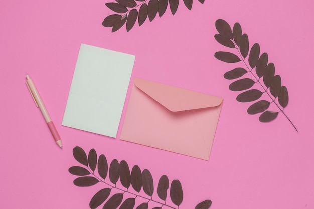 Envelope with a letter and pen on pink background with green
leaves valentines day wedding or birthday top view