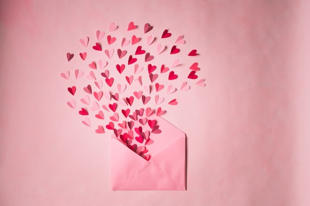 Photo envelope with paper hearts on a pink background. hearts take off from inside open envelope. romantic love letter.