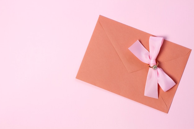 An envelope with a pink bow on a pastel pink background.