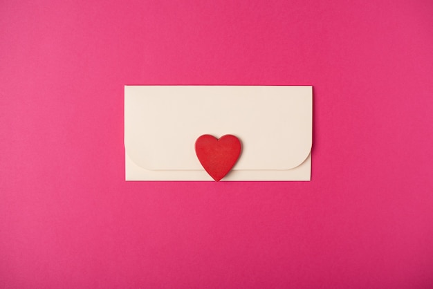 An envelope with a red wooden heart on it. Flat lay, top view. Romantic love letter for Valentine's day concept.