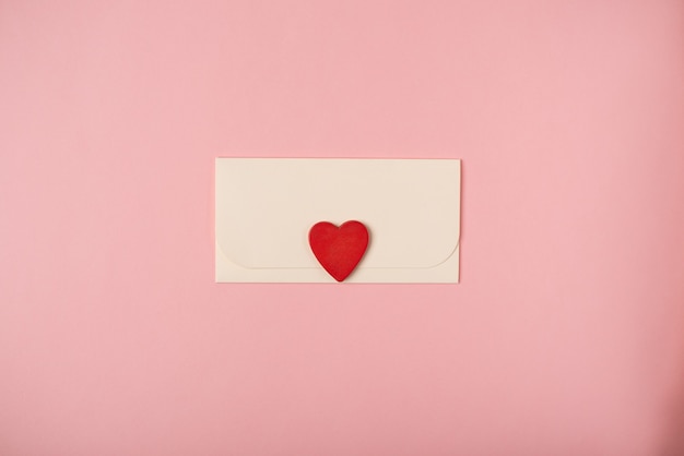 Конверт с красным деревянным сердечком. Романтическое любовное письмо для концепции дня святого Валентина. Плоская планировка, вид сверху.