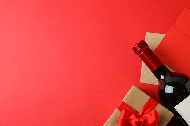 Envelopes, gift box and bottle of wine on red background