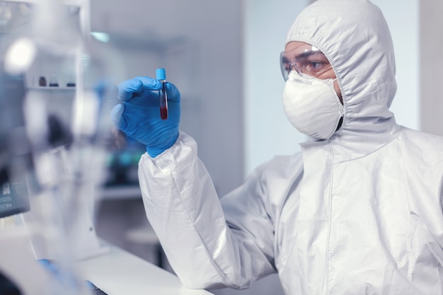 Epidemiologist analysing blood in test tube infected with coronavirus dressed in ppe suit. Doctor working with various bacteria and tissue, pharmaceutical research for antibiotics against covid19.