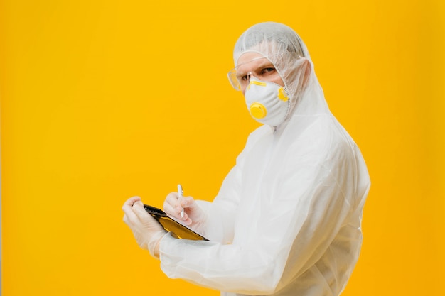 epidemiologist in a mask and hazmat suit on yellow wall writing