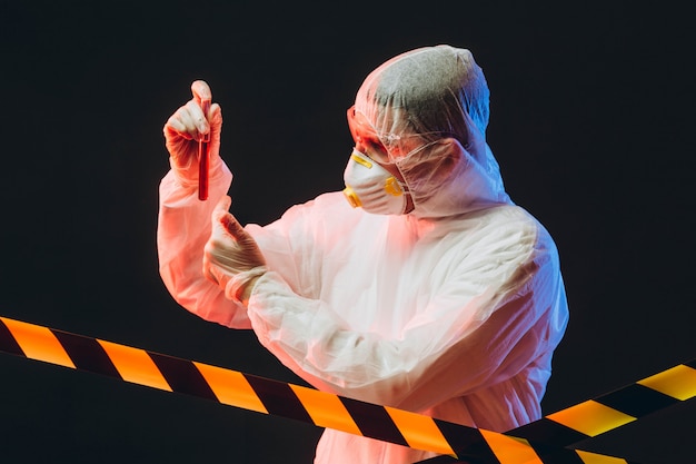 Epidemiologist on protective clothes at restricted area holding a test tube