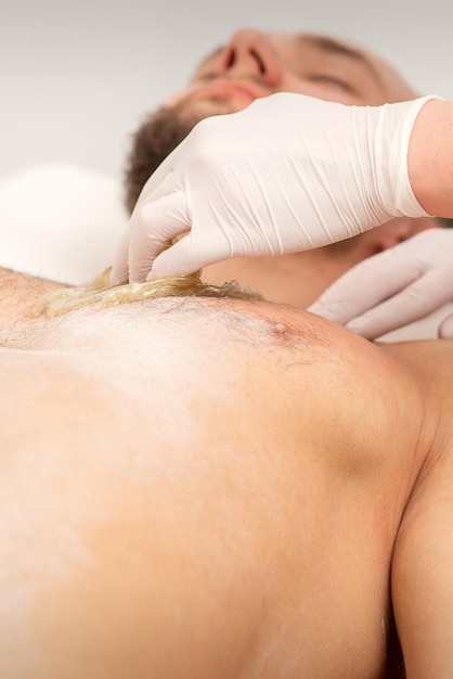 Epilation chest of a young male with the liquid wax paste in a beauty salon.