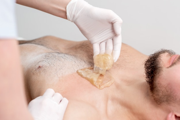 Epilation chest of young male with liquid wax paste by hands of female cosmetologist in beauty salon