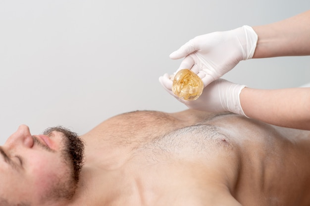 Epilation chest of young male with liquid wax paste by hands of female cosmetologist in beauty salon