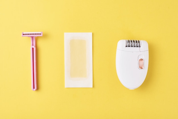 Epilator, razor and wax strips on yellow surface