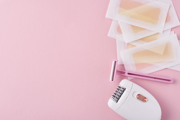 Epilator, scheermes en wax strips op roze oppervlak