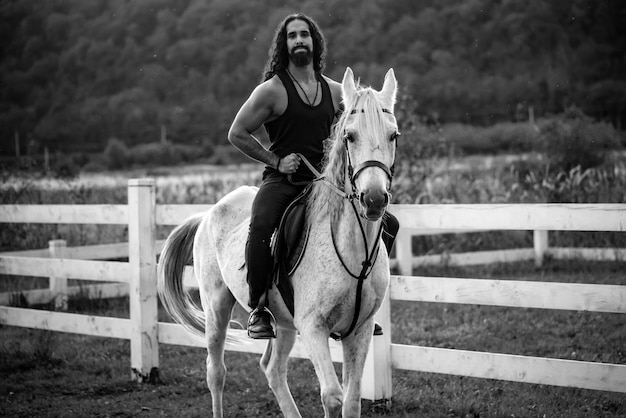 Equestrian and animal love concept rider on gray arabian horse in the field handsome bearded man rid