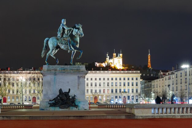 Equestrian statue of Louis XIV on the Place Bellecour, Basilica of Notre-Dame de Fourviere on the background at night in Lyon, France