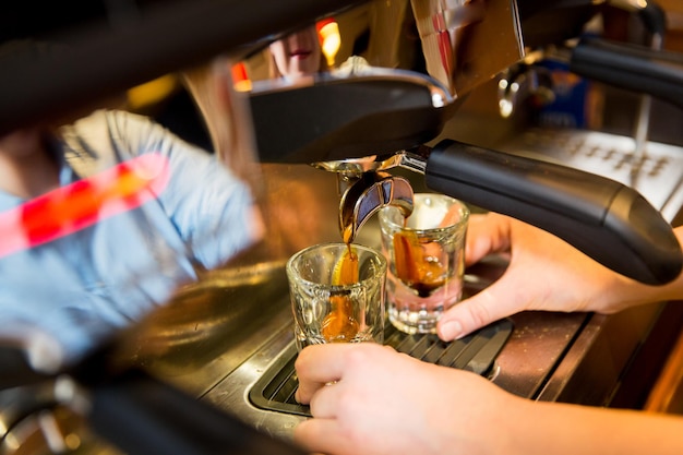 equipment, coffee shop, people and technology concept - close up of woman making coffee by espresso machine at cafe bar or restaurant kitchen