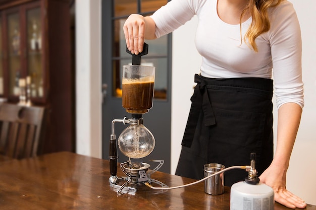equipment, coffee shop, people and technology concept - close up of woman stirring coffee grounds in siphon coffeemaker top vessel at cafe bar or restaurant kitchen