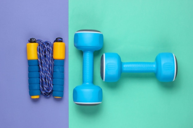 Equipment for training on colored background. Skipping rope, dumbbells. Flat lay style. Copy space