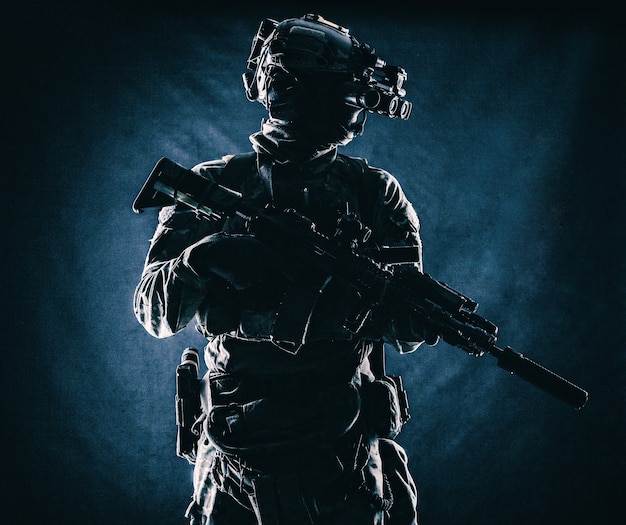 Equipped modern ammunition, armed assault rifle with silencer,
standing in darkness with four lenses night vision goggles on
battle helmet commando soldier low key, studio portrait on black
background