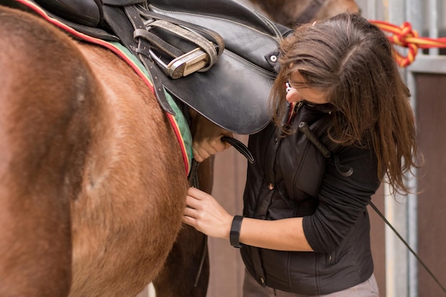 乗馬学校パドック牧場厩舎での馬術トレーニング ライダーのプロのアスリートがあぶみ乗馬用具を準備する