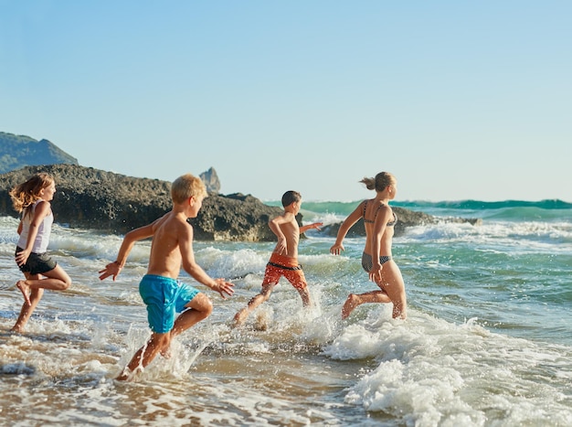 Er bestaat niet zoiets als het perfecte moment, ga nu Shot van broers en zussen die op een zonnige dag het water in rennen op het strand